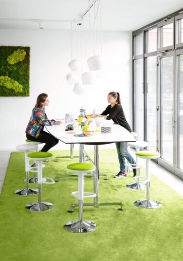 Besprechungstisch mit Hockern auf grünem Teppich im Büro Besprechungstisch mit Hockern auf grünem Teppich im Büro